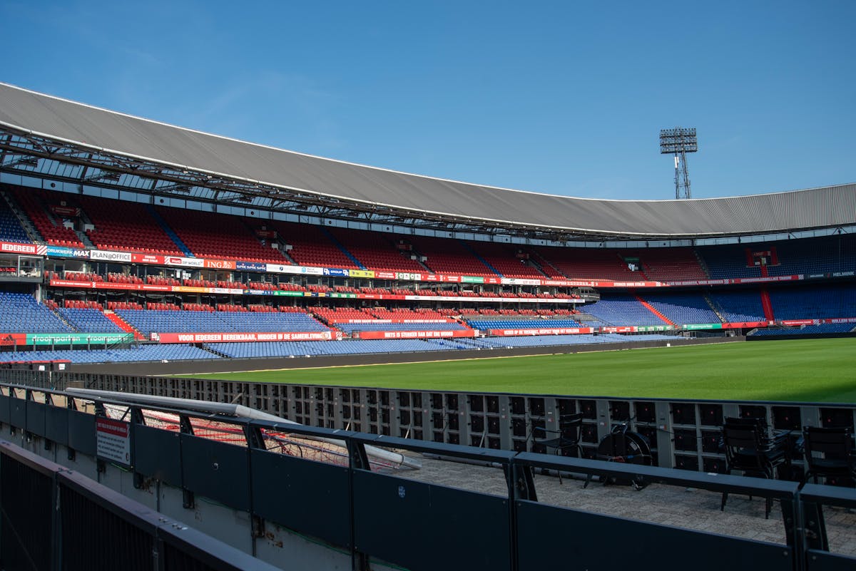 Panoramic view of De Kuip stadium in Rotterdam with empty stands and a clear blue sky.