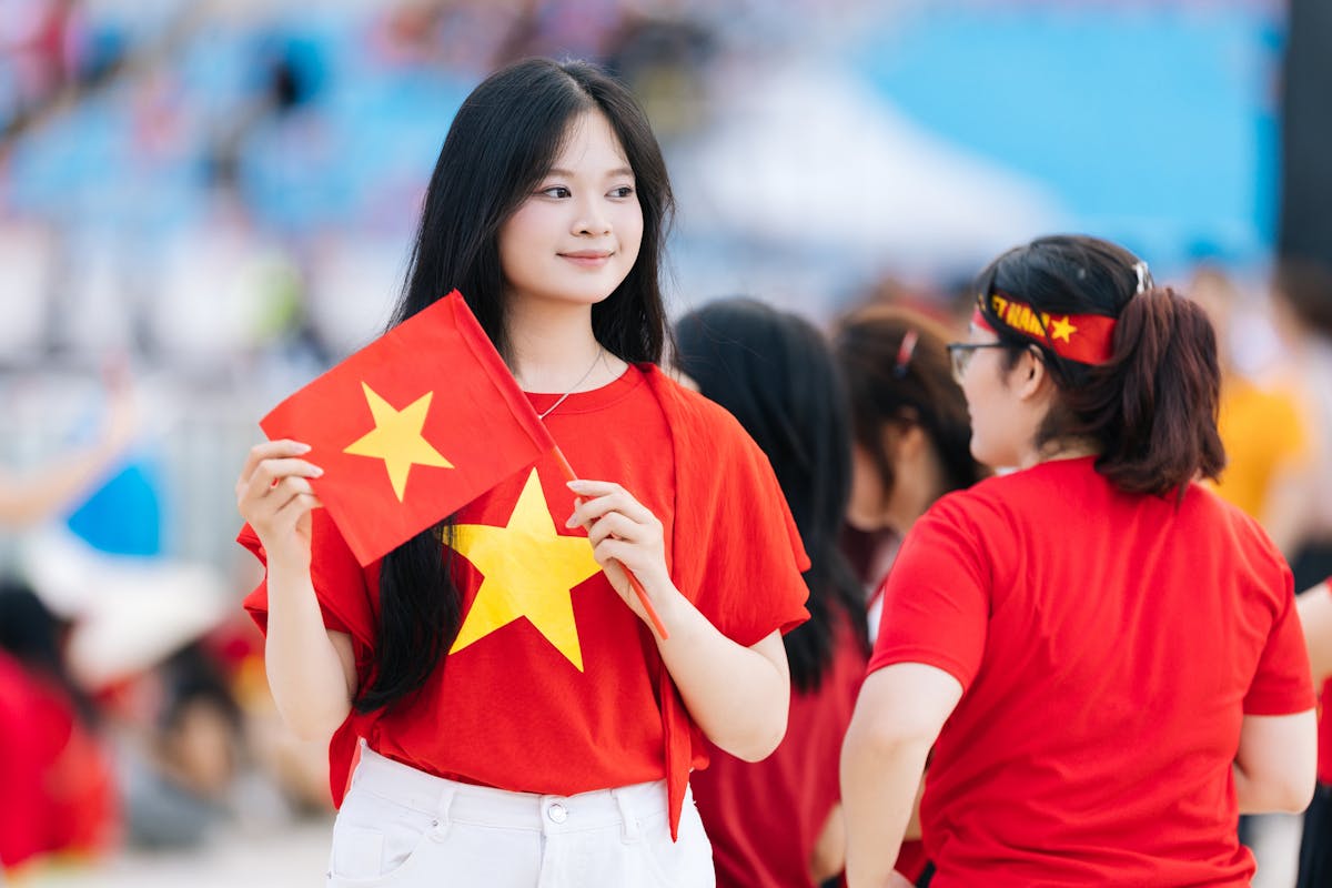 A young woman in a red t-shirt holds the Vietnam national flag, showcasing national pride at an outdoor event.