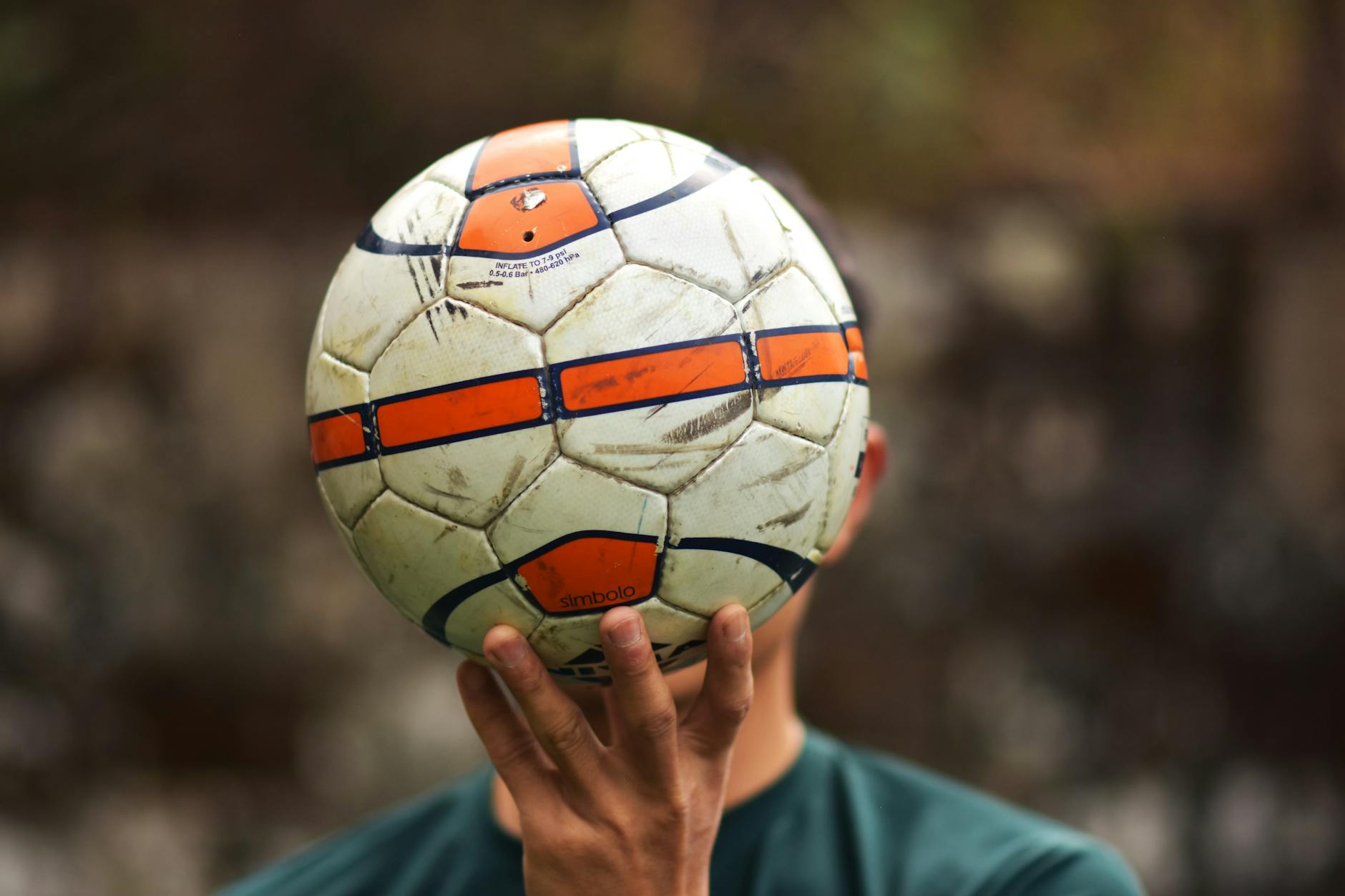 A close-up image of a hand holding a soccer ball outdoors, emphasizing sporting focus.